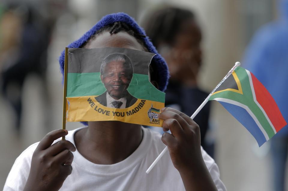 A girl covers her face with a flag bearing the image of Nelson Mandela outside of the memorial service for former South African president Nelson Mandela at the FNB Stadium in Soweto, near Johannesburg, South Africa, Tuesday Dec. 10, 2013. (AP Photo/Tsvangirayi Mukwazhi)