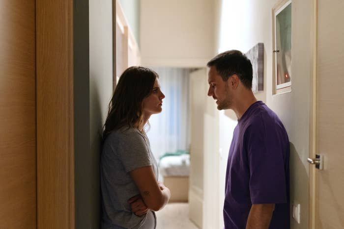 Woman and man standing face-to-face in a narrow hallway, appearing to have a serious conversation