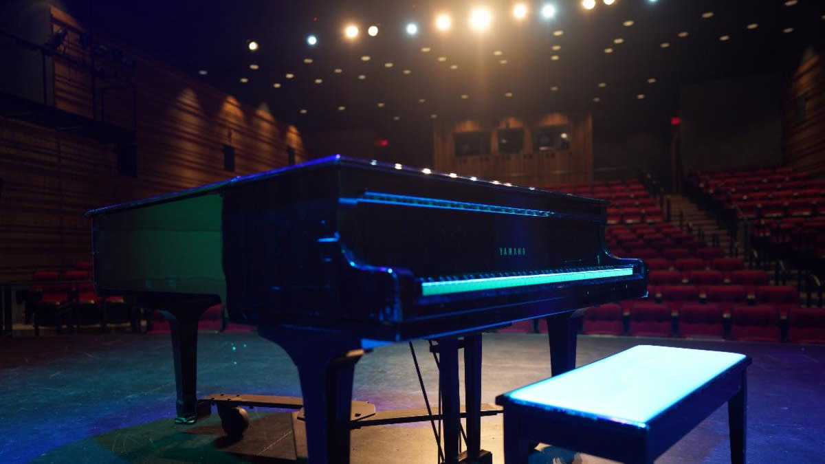  A piano shines on stage at Ontario venue with spotlights behind it. . 
