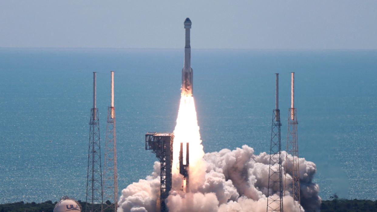  A white rocket launches on a sunny day above a plume of fire and smoke. 