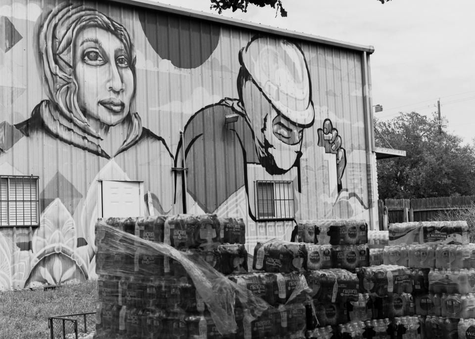 Water bottles stacked outside of the Workers Defense Project headquarters in Austin, Texas, with a mural by Trust Your Struggle Collective. At the beginning of March, 390,000 Texans were still under boil-water advisories after the winter storm.