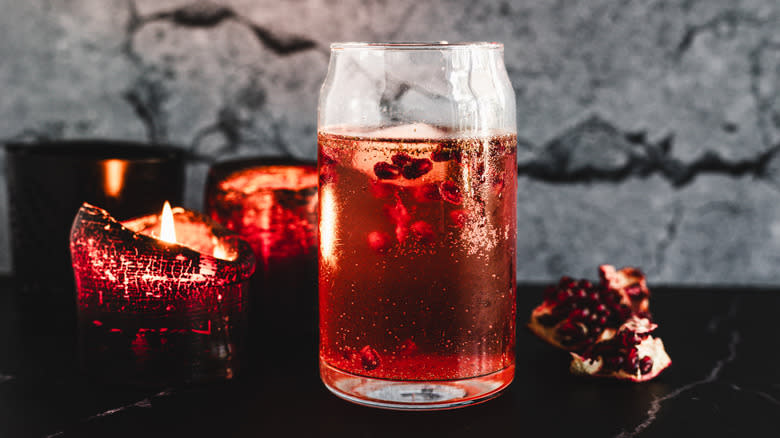 Red cocktail glass in front of candles and pomegranate