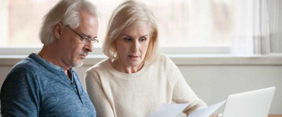 Serious senior couple looking at bills while sitting in front of laptop