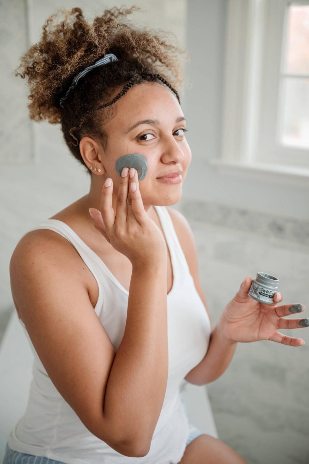 girl applying charcoal mud mask in white bathroom