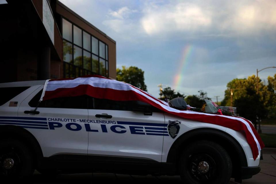 A rainbow is seen behind the police vehicle that draped in an American flag outside the police station on North Tryon on Tuesday, April 30, 2024. Flowers have been placed on the hood in memory of CMPD officer Joshua Eyer, who was killed in yesterday’s deadly shootout in East Charlotte.