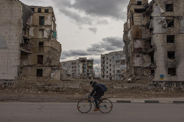 A man rides a bicycle past destroyed residential buildings.