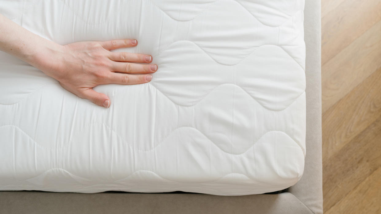  A person places their hand on top of a white mattress to check for sagging. 
