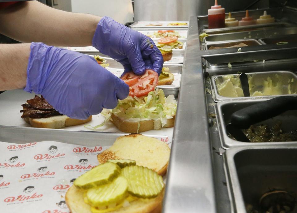 Dylan Pierce dresses a burger in the kitchen at Wink's Drive-In in Barberton on Tuesday, April 18, 2023.