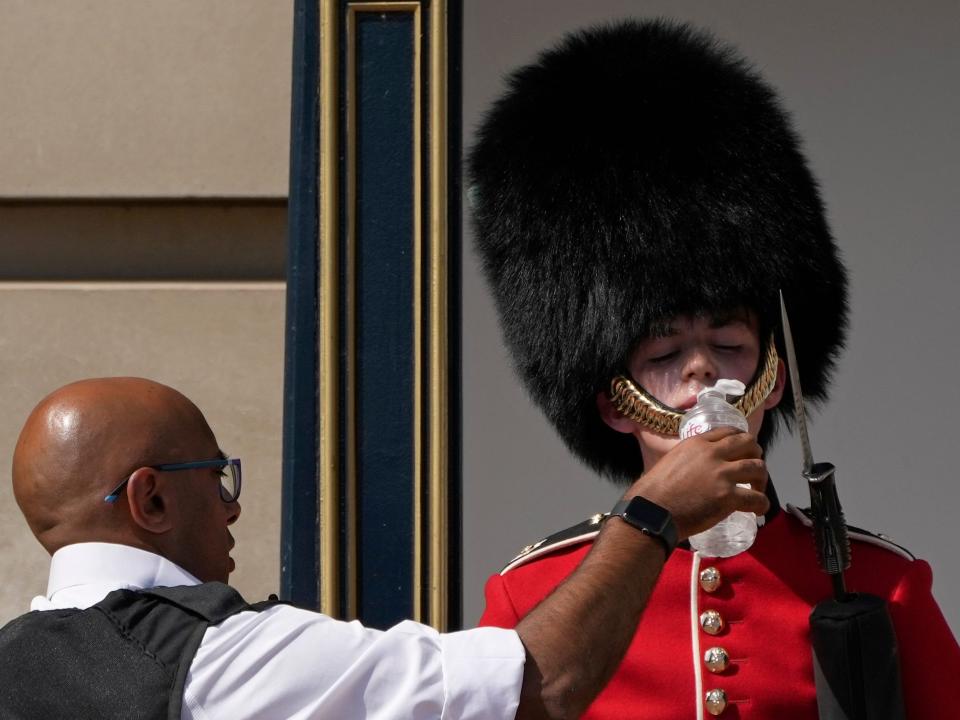 A police officer pours water into the mouth of a British soldier outside Buckingham Palace.