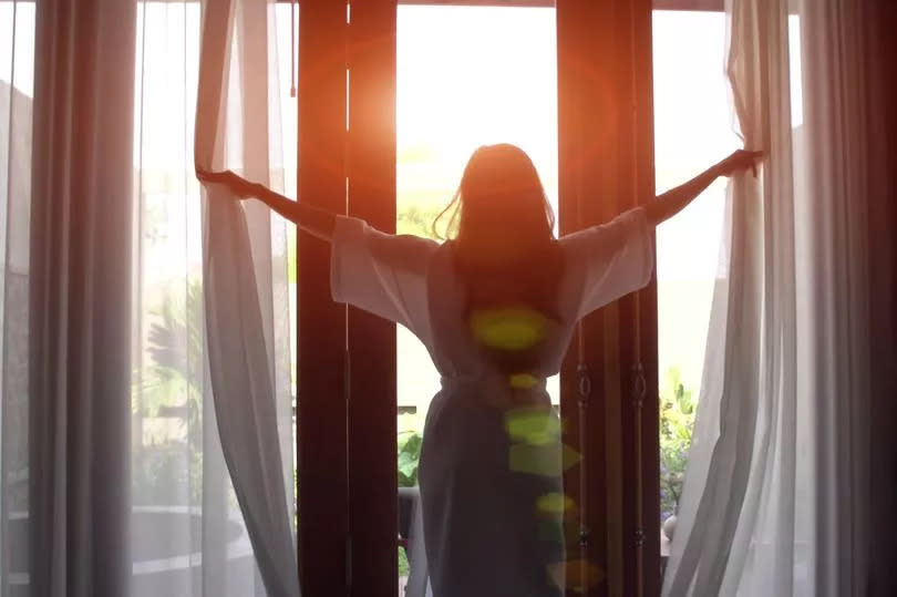 Young woman opening curtains in the morning