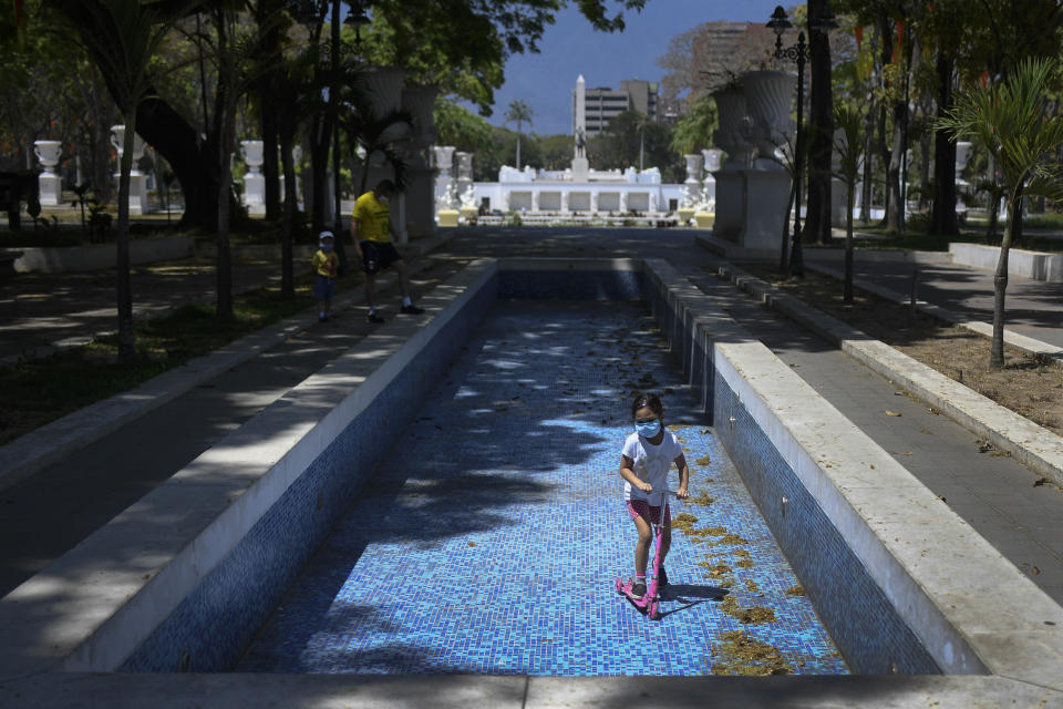 Una niña, con mascarilla para protegerse del coronavirus, juega con su patinete dentro de una fuente vacía en el paseo de Los Próceres, en Caracas, Venezuela, el 26 de abril de 2020. Se estima que el 86% de los venezolanos reportó problemas con el suministro de agua, incluyendo un 11% que no tiene, según una encuesta realizada por la ONG Observatorio Venezolano de Servicios Públicos entre 4.500 residentes en abril. (AP Foto/Matías Delacroix)