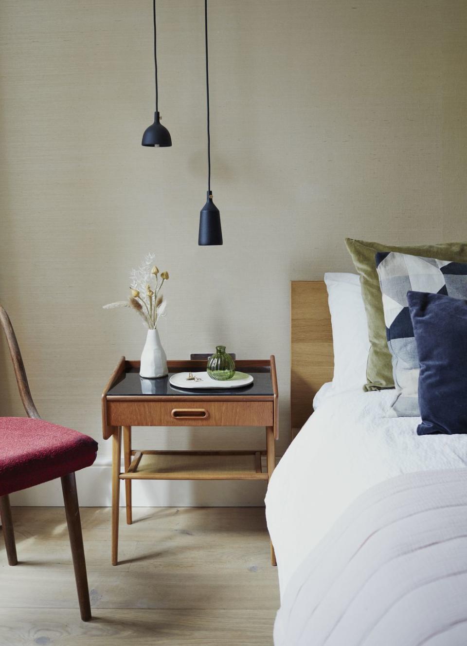 a bedroom in neutral colours with wooden floors, off white walls, mid century style side table and wooden bed frame with white bed linen