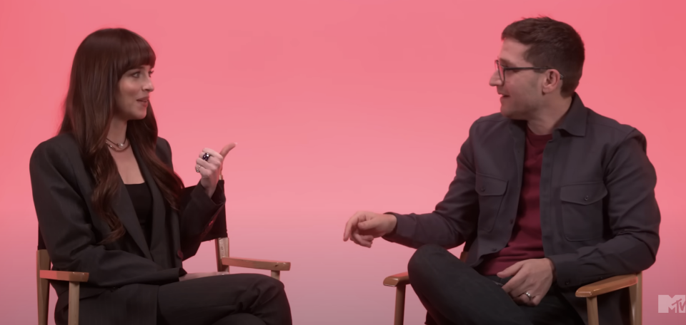 Dakota and Josh sitting, chatting, one gesturing with hand; they're in front of a pink background