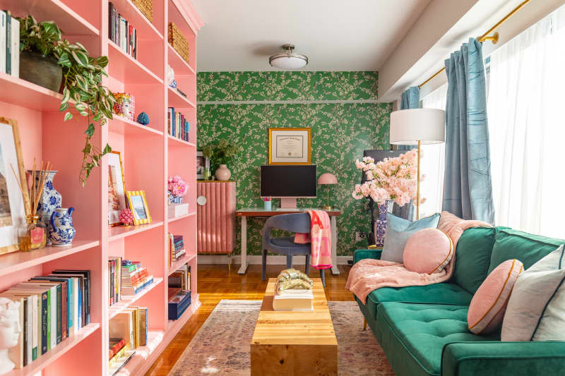 A living room with a green fabric couch across from a pink bookcase and gallery wall