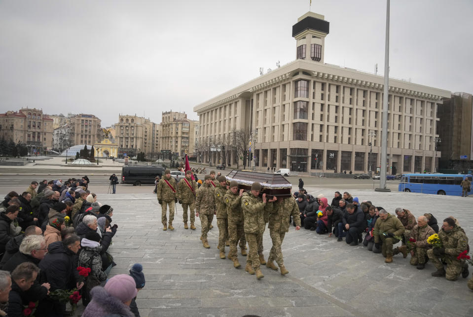 People kneel as the Ukrainian servicemen carry the coffin of their comrade Oleh Yurchenko killed in a battlefield with Russian forces in the Donetsk region during a commemoration ceremony in Independence Square in Kyiv, Ukraine, Sunday, Jan. 8, 2023. (AP Photo/Efrem Lukatsky)