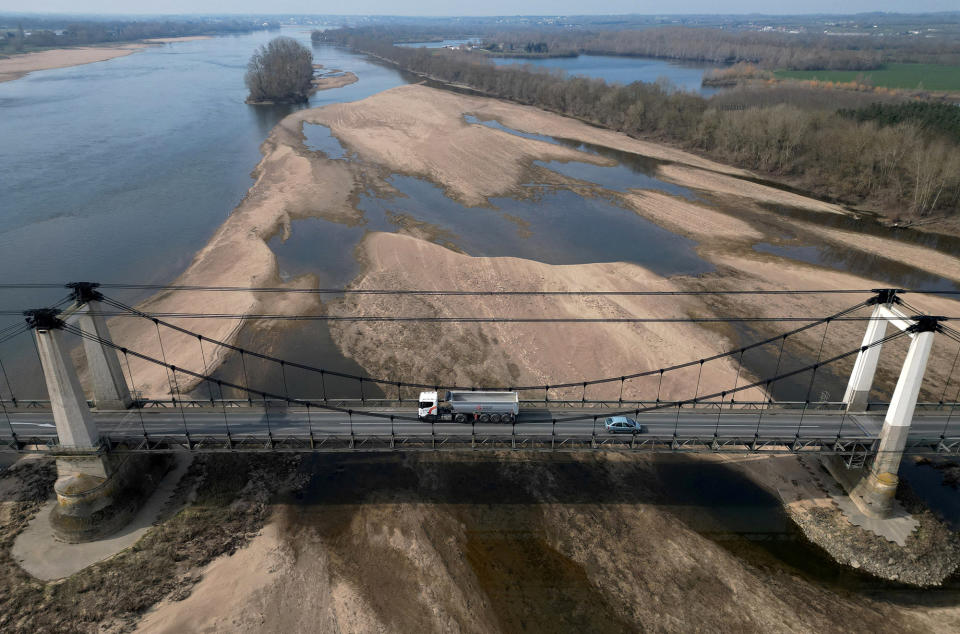 An aerial view of a freight truck and car driving in opposite directions over a bridge above a drying river's sandbanks