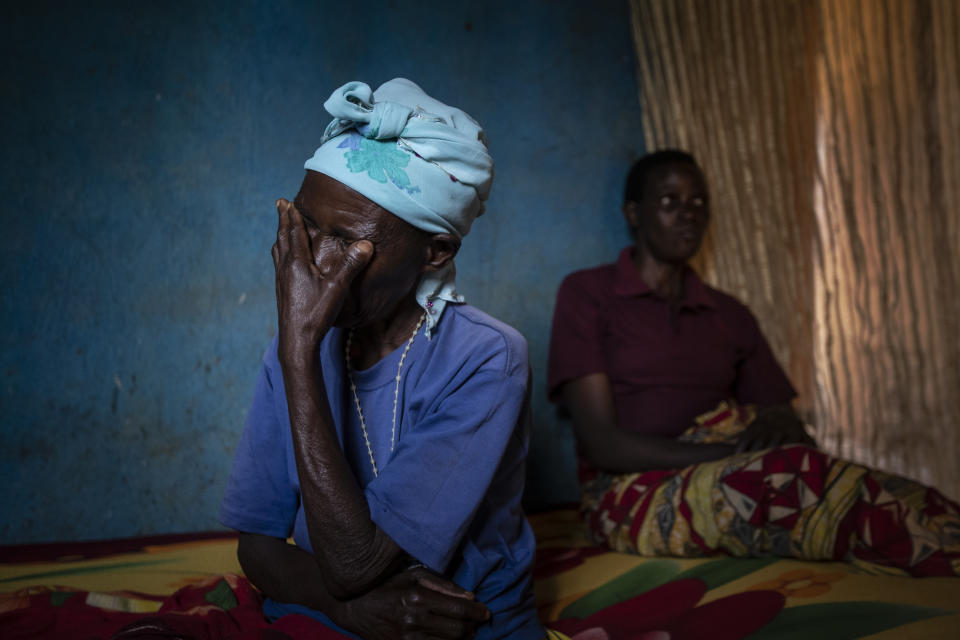 In this photo taken Monday, Nov. 4, 2019, cancer patient Athanasie Nyirangirababyeyi, 89, left, who is taking oral liquid morphine for her pain, holds her face, accompanied by her daughter-in-law Maria Mukamabano, right, during a visit to check on her health by palliative care nurse Madeleine Mukantagara at her son's home in the village of Kagano, near Kibogora, in western Rwanda. While people in rich countries are dying from overuse of prescription painkillers, people in Rwanda and other poor countries are suffering from a lack of them, but Rwanda has come up with a solution to its pain crisis - it's morphine, which costs just pennies to produce and is delivered to households across the country by public health workers. (AP Photo/Ben Curtis)