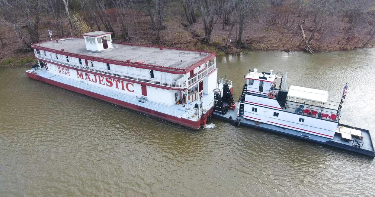 Showboat Majestic, a fixture on Cincinnati's Public Landing from 1967 to 2019, is now tied up near Portsmouth, Ohio, on the Kentucky side of the Ohio River with its towboat, the Miss Anne. Nearby are buildings, on the Kentucky shore, once used to maintain an old river dam.