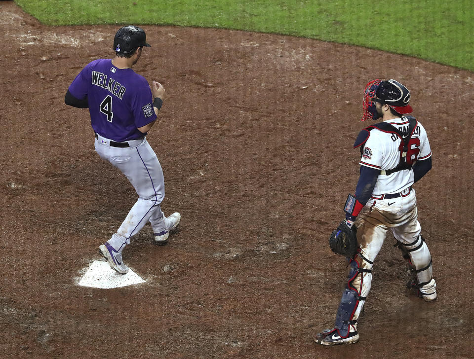 Colorado Rockies' Colton Walker scores the go-ahead run next to Atlanta Braves catcher Travis d'Arnaud during the 10th inning of a baseball game Wednesday, Sept. 15, 2021, in Atlanta. (Curtis Compton/Atlanta Journal-Constitution via AP)