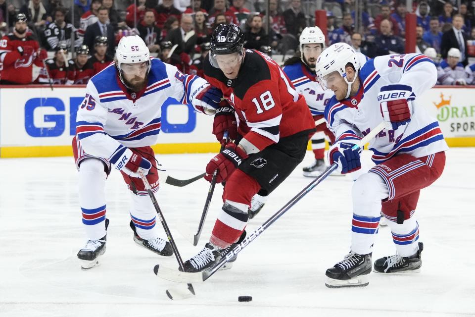 New Jersey Devils' Ondrej Palat (18) and New York Rangers' Adam Fox (23) and Ryan Lindgren (55) reach for the puck during the second period of Game 5 of an NHL hockey Stanley Cup first-round playoff series Thursday, April 27, 2023, in Newark, N.J. (AP Photo/Frank Franklin II)