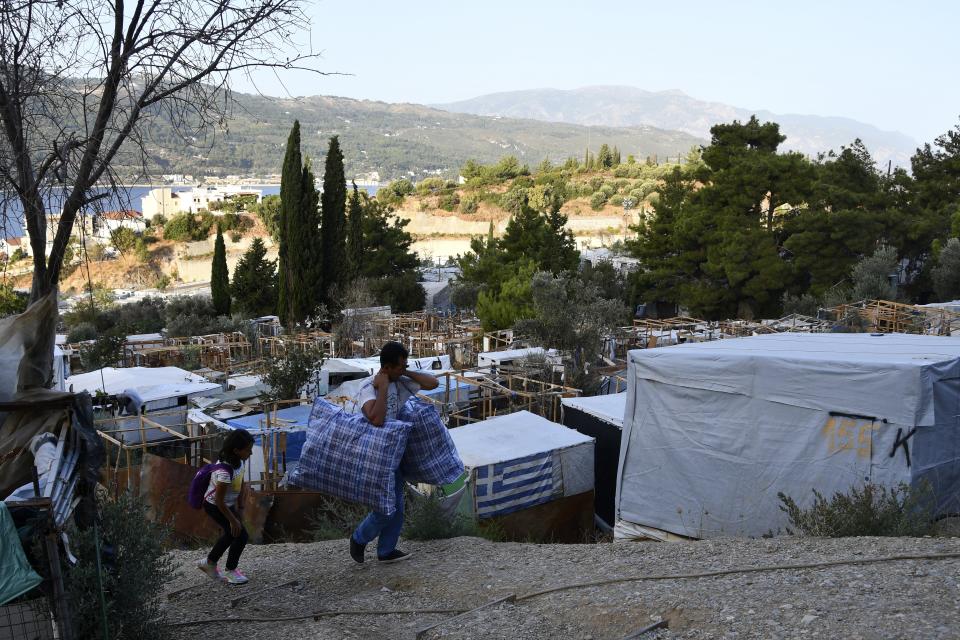 Migrants carry their belongs as they leave from an overcrowded refugee camp at the port of Vathy on the eastern Aegean island of Samos, Greece, Monday, Sept. 20, 2021. The transfer of all the migrants to the new €43 million ($50 million) closed monitored facility began Monday and be completed by Wednesday. (AP Photo/Michael Svarnias)