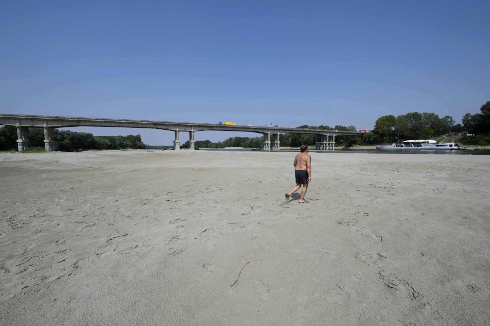 A man walks near a bridge in Boretto, Italy, on the bed of the Po river, Wednesday, June 15, 2022. The drying up of the river is jeopardizing drinking water in Italy's densely populated and highly industrialized districts and threatening irrigation in the most intensively farmed part of the country. (AP Photo/Luca Bruno)