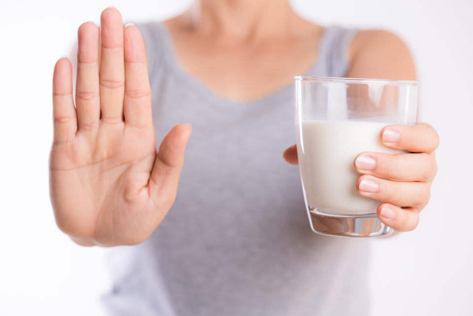 Woman hand holding glass of milk while putting her other hand up saying stop.