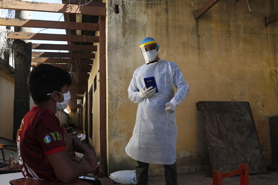 A youth in quarantine is interviewed by a member of the National Mechanism to Prevent Torture (MNPT) at a school being used as a government-run shelter where citizens returning home are required by law to quarantine for two weeks and pass two consecutive COVID-19 tests, as a preventive measure amid the COVID-19 pandemic in Ciudad del Este, Paraguay, Thursday, June 24, 2020. The youth said he'd been there for two months. While Paraguay appears to be controlling the disease, it faces concerns about a predicted 5% drop in gross domestic product for an economy that was already struggling, and a health system that remains unprepared for a large-scale epidemic. (AP Photo/Jorge Saenz)