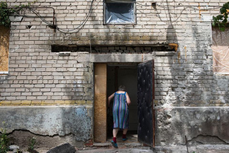 A woman walks into a home that has sustained shell damage in the village of Novoluganskoe. Eastern Ukraine is full of pensioners who have stayed behind, often due to a lack of money or physical strength.