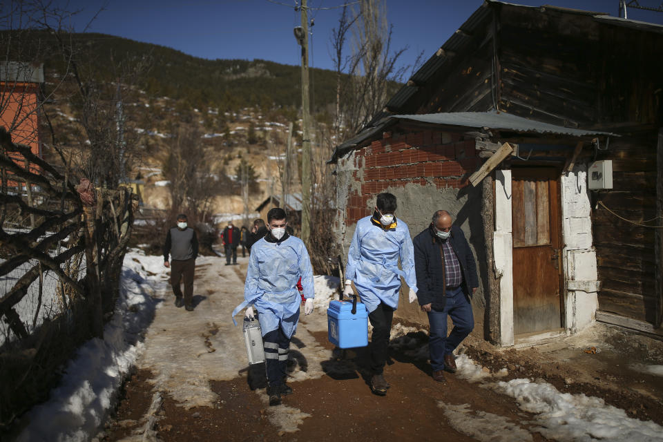 Dr. Yasin Kaya, center and health worker Yusuf Duran, left, members of the the Koyulhisar Public Health Center vaccination team, walk to vaccinate 85-year-old Ibrahim Yigit at his house in the isolated village of Gumuslu in the district of Sivas, central Turkey, Friday, Feb. 26, 2021. (AP Photo/Emrah Gurel)