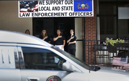 Workers from a local restaurant workers stand beneath a sign with their hands on their hearts, as a hearse carrying the casket of slain Pennsylvania State Police Trooper Corporal Bryon Dickson, passes following his funeral service at St. Peters' Cathedral in Scranton, Pennsylvania September 18, 2014. REUTERS/Mike Segar