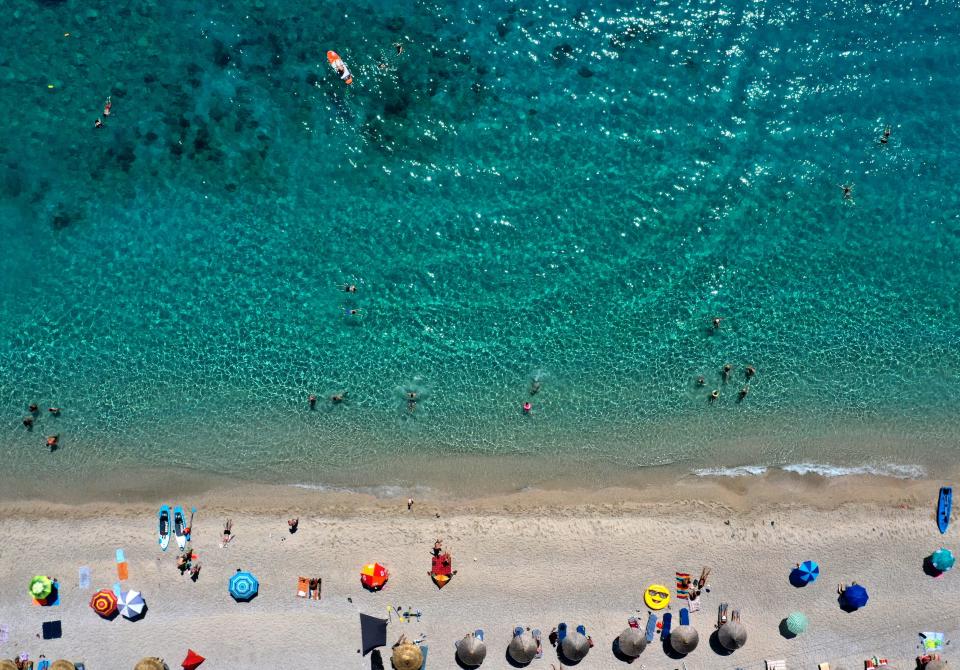 This aerial view taken on August 6, 2019, shows tourists, parasols and buoys on the beach of Llaman, near the city of Himare. - The hot weather conditions of the last days in Albania have seen temperatures reach a peak of 37 degrees Celsius. (Photo by Gent SHKULLAKU / AFP)        (Photo credit should read GENT SHKULLAKU/AFP/Getty Images)