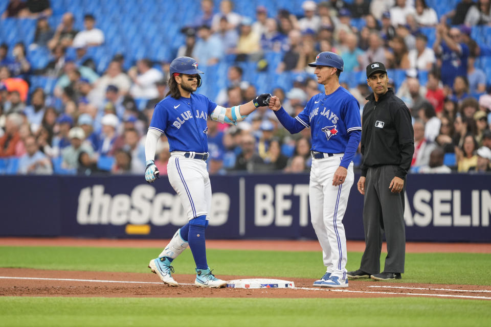 Toronto Blue Jays' Bo Bichette, left, celebrates a single with first base coach Mark Budzinski, center, against the Houston Astros in first-inning baseball game action in Toronto, Ontario, Monday, June 5, 2023. (Andrew Lahodynskyj/The Canadian Press via AP)