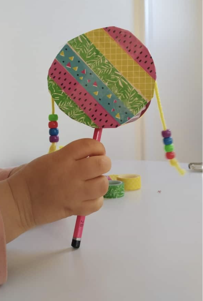 crafts for kids, child holding a hand drum decorated with washi tape, beads and yarn