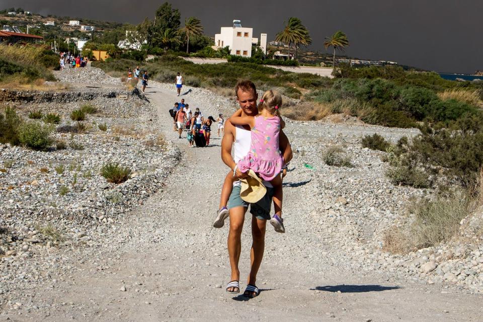 A man carries a child as they leave an area where a forest fire burns, on the island of Rhodes, Greece, Saturday, July (AP)