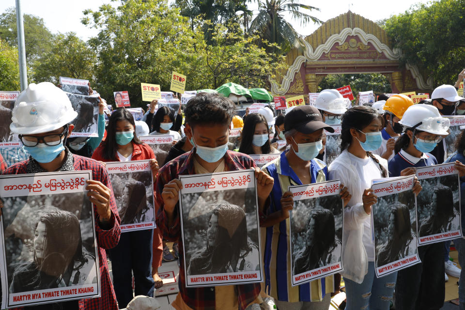 FILE - In this Feb. 14, 2021, file photo, Mandalay University graduates bow their heads as they hold posters with images of Mya Thwet Thwet Khine, a young woman who was shot in the head by police during a protest on Feb. 9 in Naypyitaw, at an anti-coup protest in Mandalay, Myanmar. The woman shot by police during a protest against the military’s takeover of power died Friday morning, Feb. 19, 2021, her brother said. (AP Photo, File)