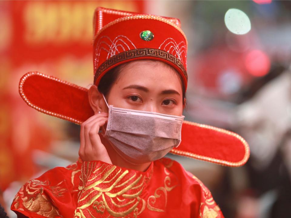 A woman in costume of the Prosperity and Wealth God wears a protective face mask at a gold shop in Hanoi, Vietnam, Monday, Feb. 3, 2020.