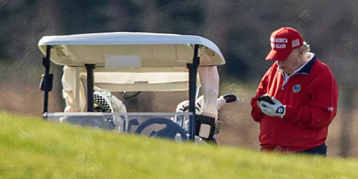 Trump in red next to golf car tapping his phone