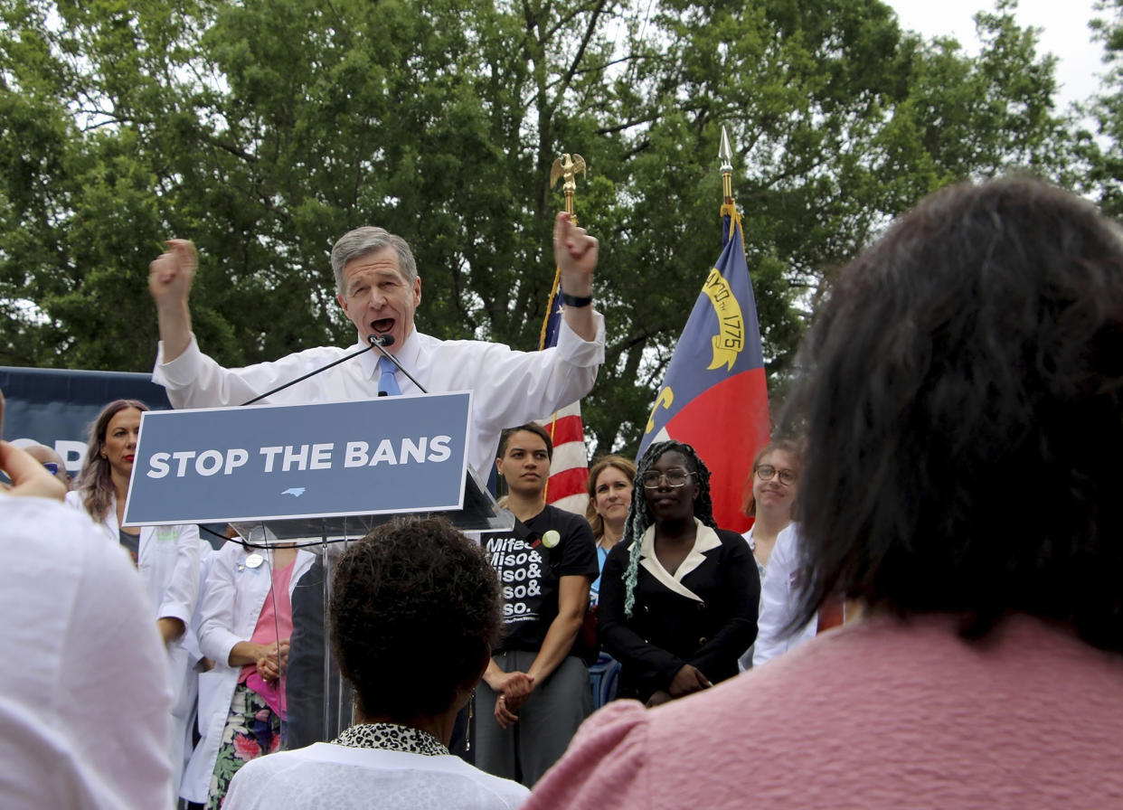 North Carolina Governor Roy Cooper stands at a podium as he speaks to a crowd of abortion rights supporters. A sign in front of him reads: Stop the bans.