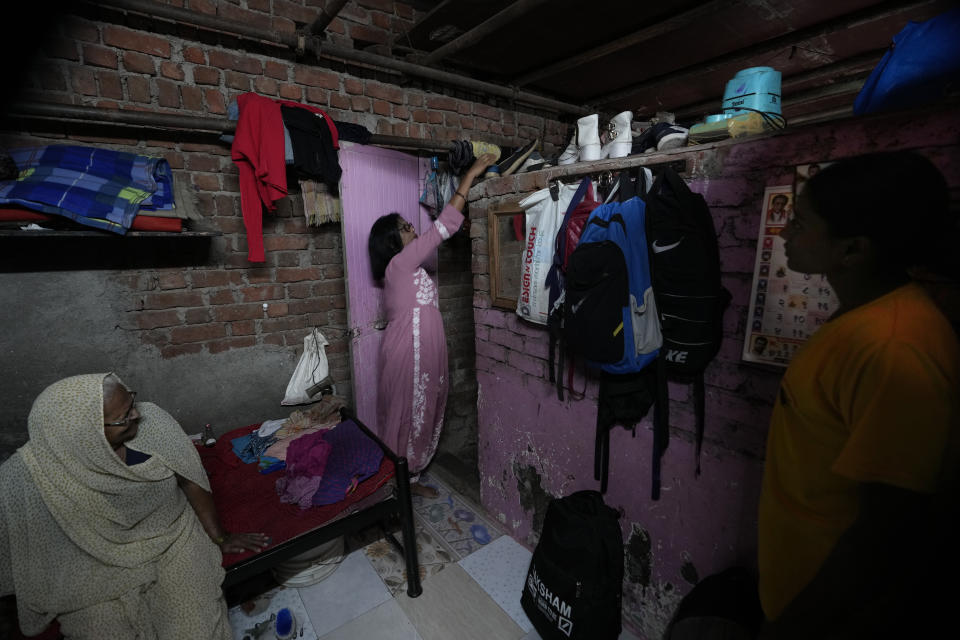 Lalmani Chauhan reacts for her shoes before leaving for office, watched by family members, at her home in a slum in Mumbai, India, Friday, March 17, 2023. It was the promise of jobs and a better life that drew Chauhan to Mumbai. She is the first woman in her family to work - and the first to enroll into university, which she did recently. Her salary is putting her three children - one boy and two girls - through school. (AP Photo/Rajanish Kakade)