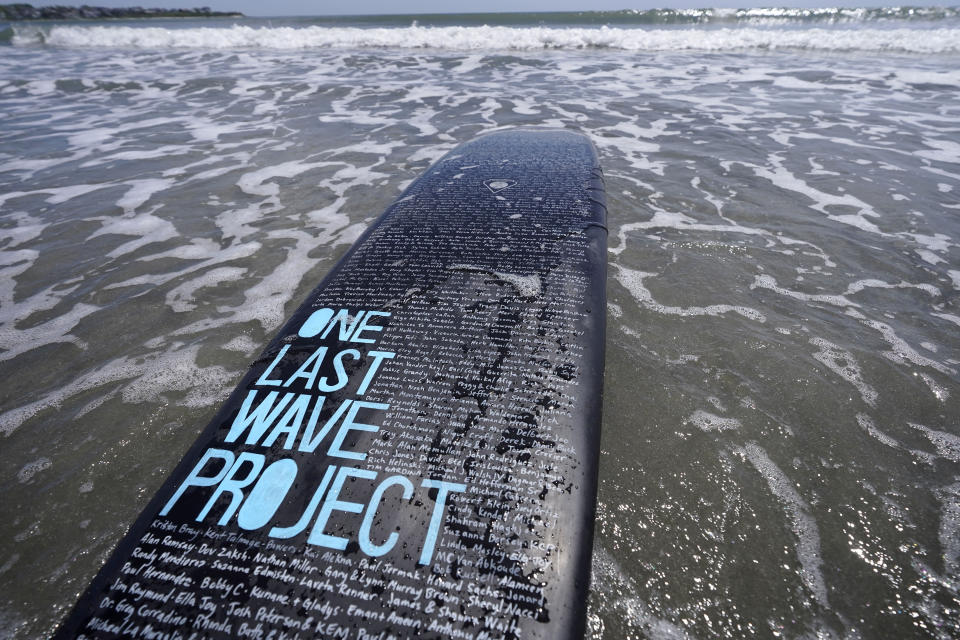 A surfboard belonging to Dan Fischer, of Newport, R.I., is covered with names of lost loved ones while resting in the water at Easton's Beach, in Newport, Wednesday, May 18, 2022. Fischer, 42, created the One Last Wave Project in January 2022 to use the healing power of the ocean to help families coping with a loss, as it helped him following the death of his father. Fischer places the names onto his surfboards, then takes the surfboards out into the ocean as a way to memorialize the loved ones in a place that was meaningful to them. (AP Photo/Steven Senne)