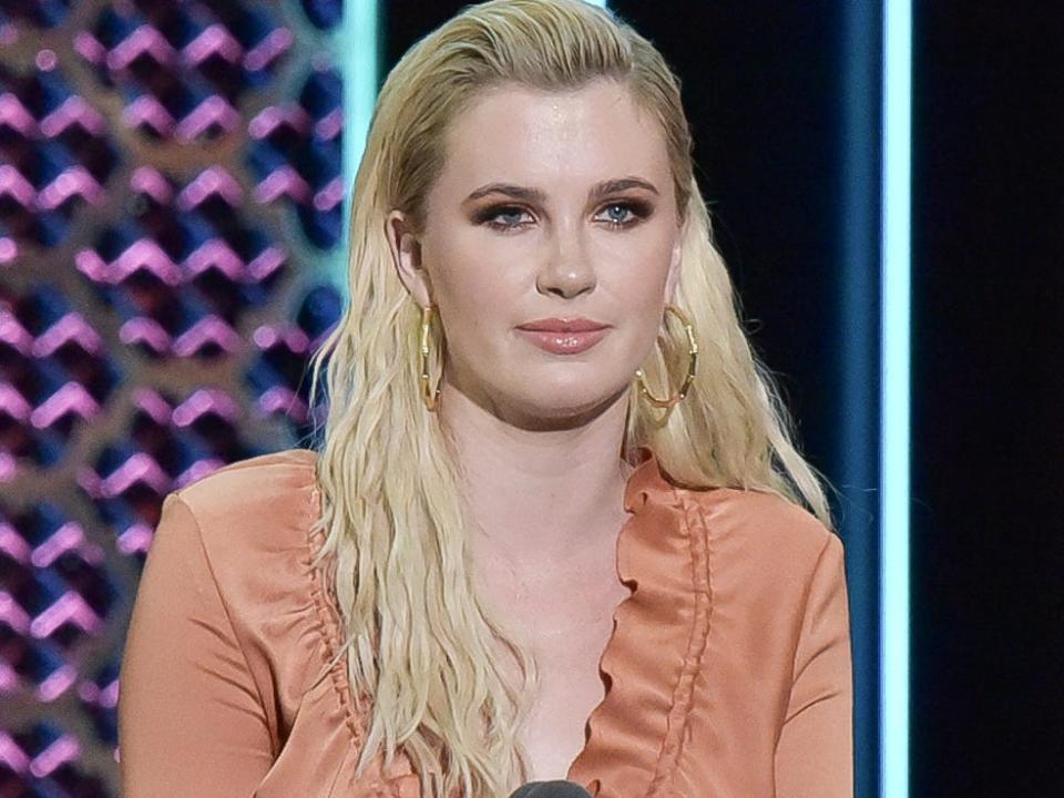 Model Ireland Baldwin wears an orange dress with long sleeves while standing on stage at the 2019 Comedy Central roast of Alec Baldwin.
