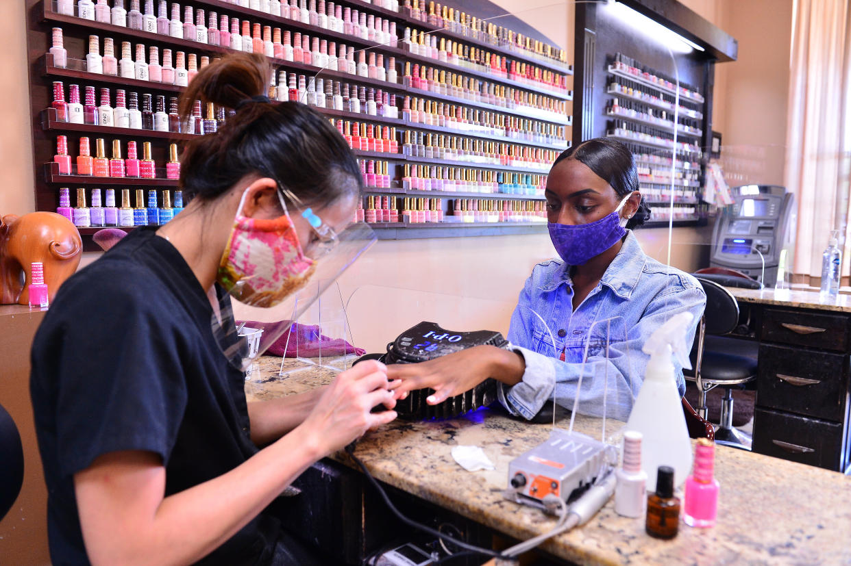 Nail technician Habe is protected by a plexiglass barrier while giving a customer a manicure at Nails and Spa salon on May 20, 2020, in Miramar, Florida.