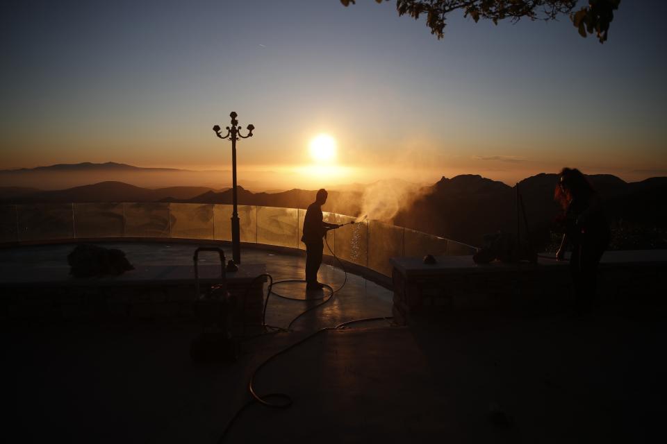 A worker cleans the balcony of an all-day cafe bar restaurant as the sun sets in Apeiranthos village, on the Aegean island of Naxos, Greece, Tuesday, May 11, 2021. With debts piling up, southern European countries are racing to reopen their tourism services despite delays in rolling out a planned EU-wide travel pass. Greece Friday became the latest country to open up its vacation season as it dismantles lockdown restrictions and focuses its vaccination program on the islands. (AP Photo/Thanassis Stavrakis)