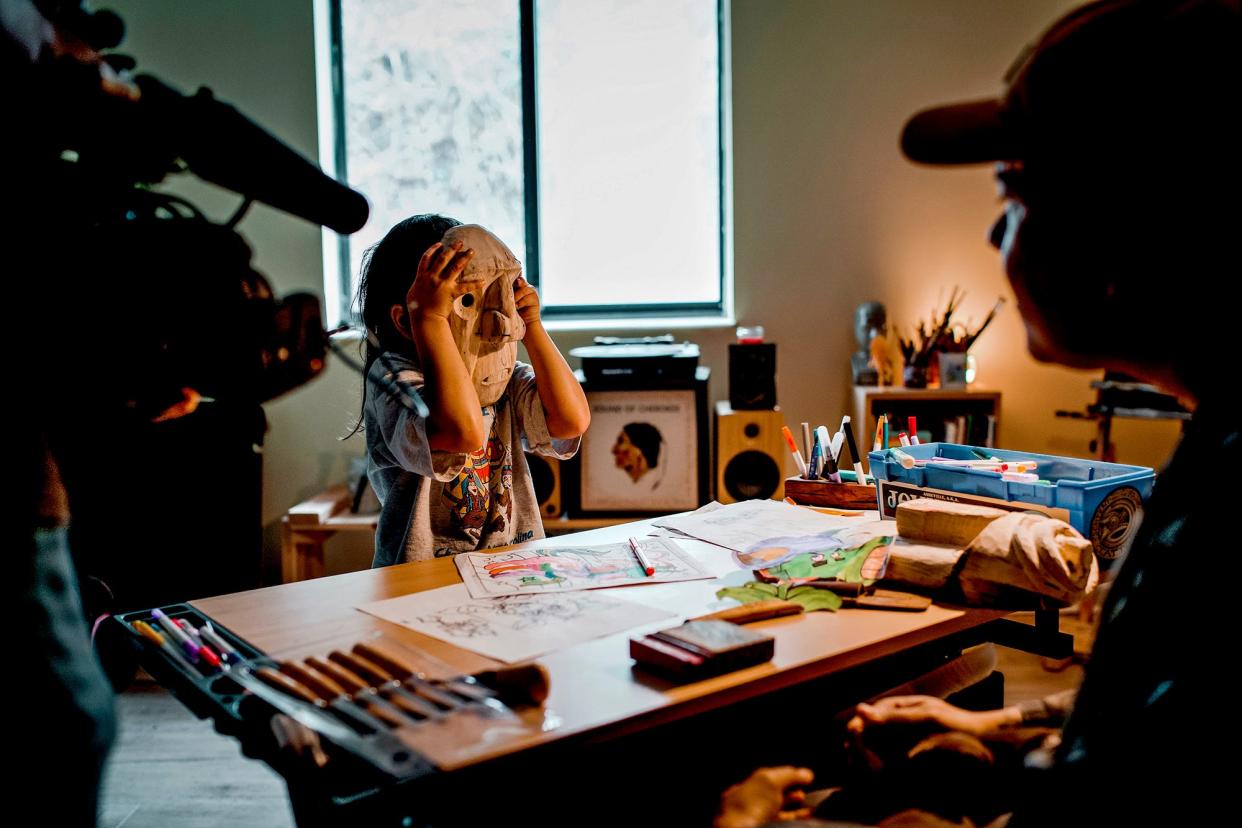 Native American artist John Henry Gloyne (Eastern Band of Cherokee Indians) watches his son, Elwood Gloyne (Eastern Band of Cherokee Indians), hold one of his booger masks mid-carving. The Gloynes are among the Cherokee people featured in Oklahoma-based Cherokee filmmaker Brit Hensel's short film "ᎤᏕᏲᏅ" (pronounced oo-de-yo-NUH).