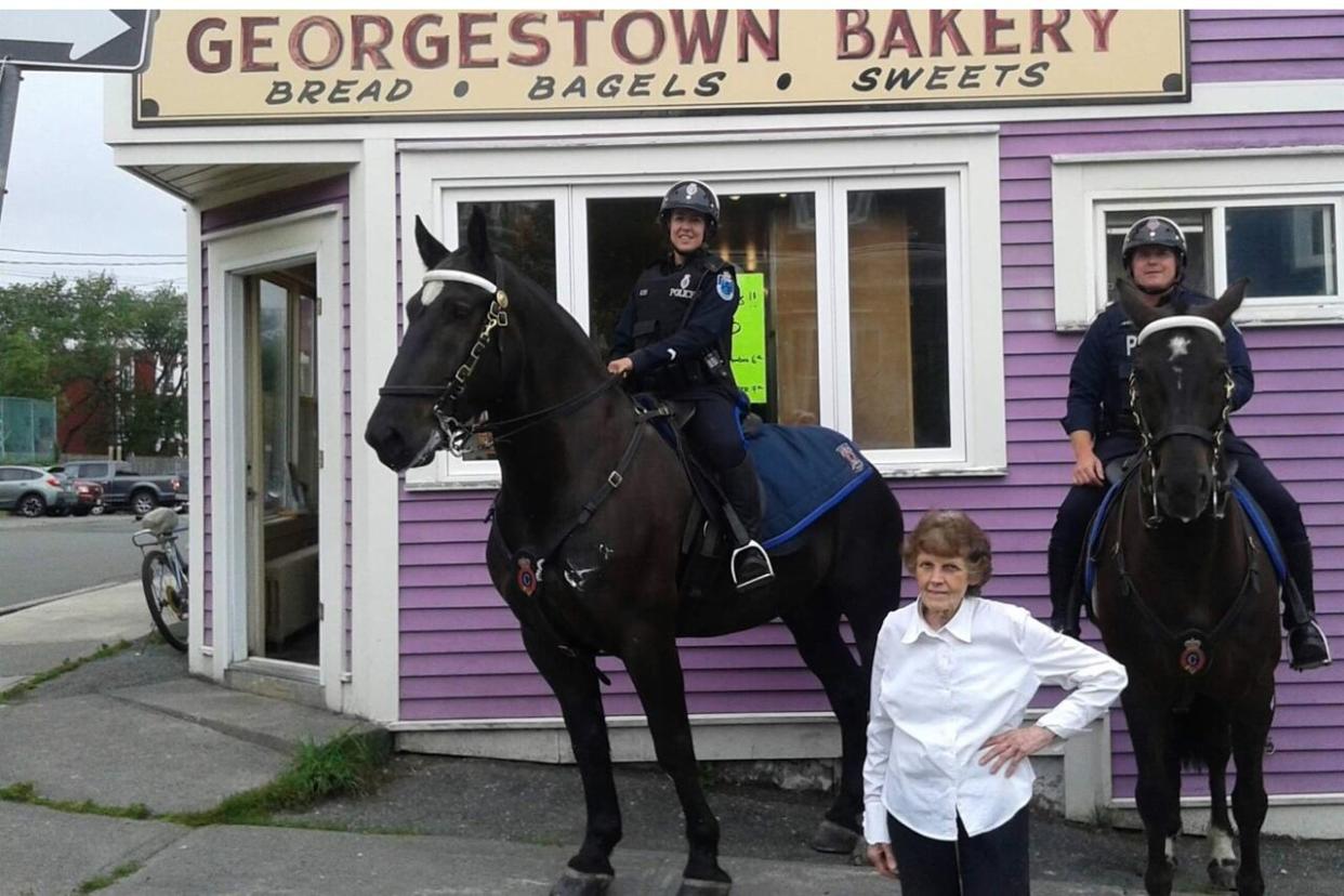 Irene Keating stands outside Georgestown Bakery with two mounted units of the Royal Newfoundland Constabulary. (Gary Cogswell/ Submitted by Stephen Lewis - image credit)