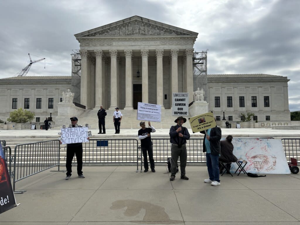 A few protesters hold signs outside the U.S. Supreme Court on April 25, 2024, during oral arguments on a presidential immunity case.
