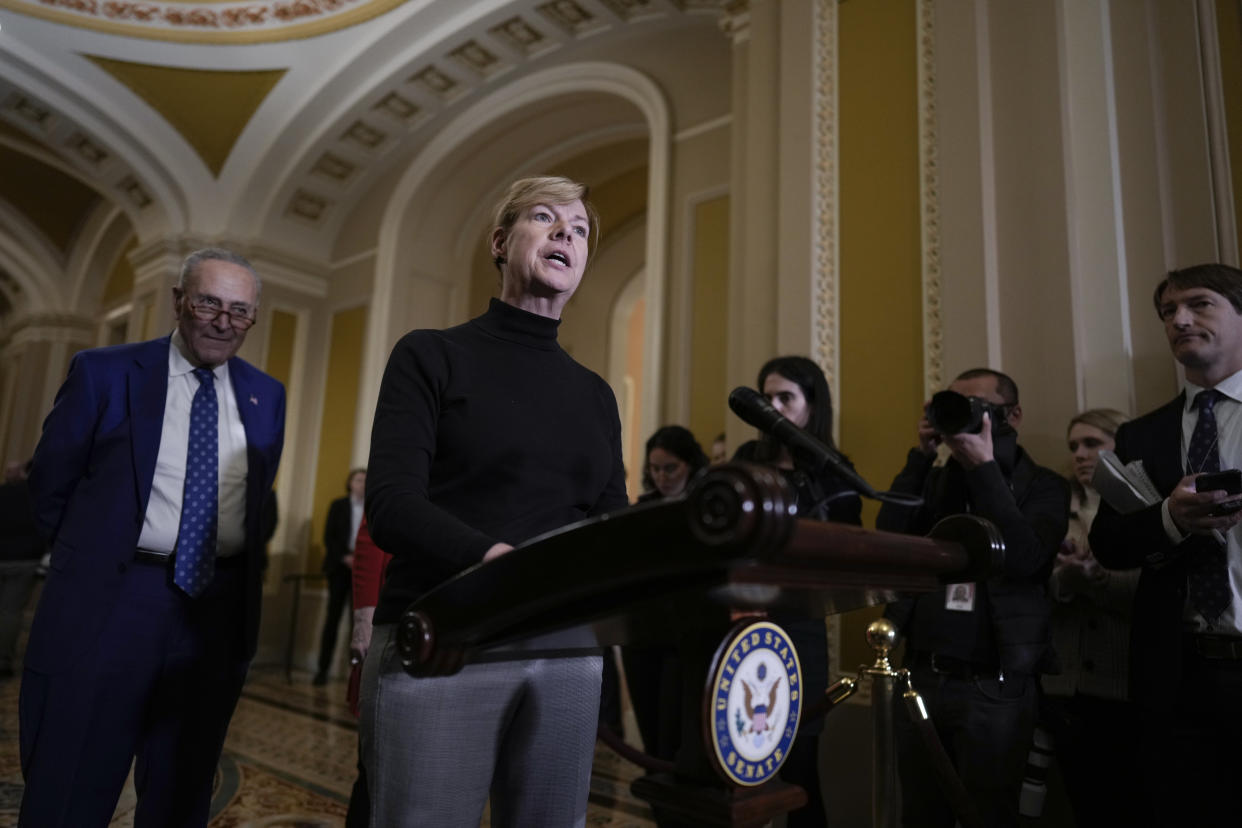 Sen. Tammy Baldwin, D-Wis., with Senate Majority Leader Chuck Schumer at her side, stands at a lectern and talks about the Respect for Marriage Act.