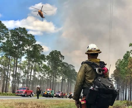 A firefighter watches a helicopter above Georgia Highway 177 as the West Mims fire burns in the Okefenokee National Wildlife Refuge, Georgia, U.S. April 25, 2017. Fish and Wildlife Service/Mark Davis/Handout via REUTERS