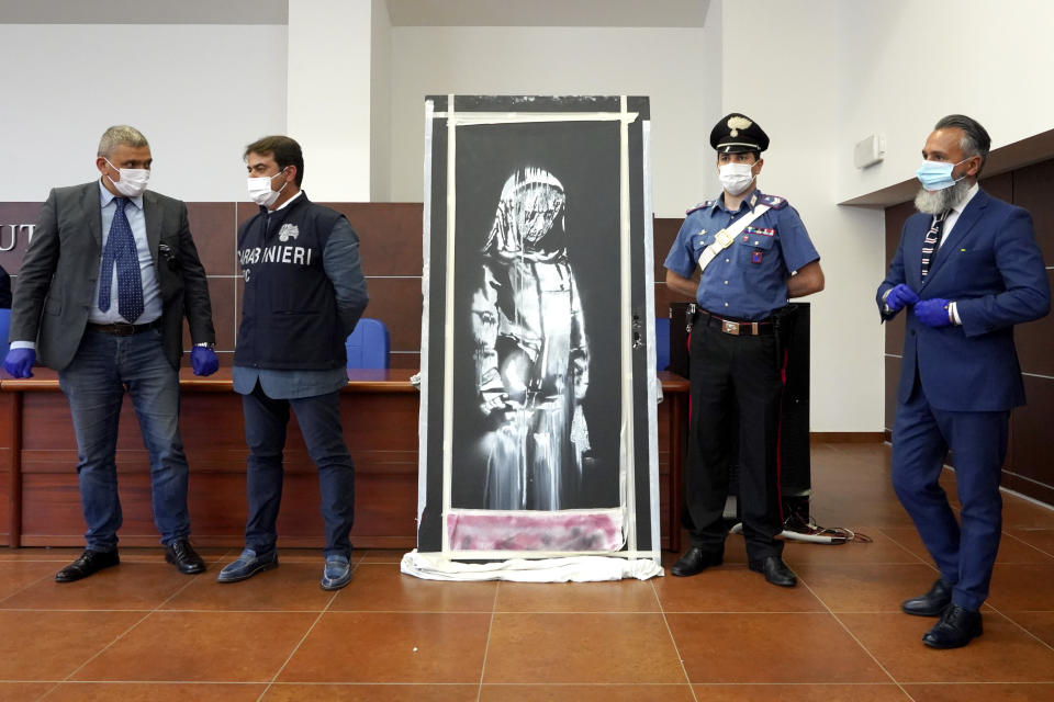 Las autoridades italianas develan una obra de arte robada del artista británico Banksy en honor a las víctimas del ataque terrorista en la sala de conciertos Bataclan en París en 2015, durante una conferencia de prensa en L' Aquila, Italia, el jueves 11 de junio de 2020. Las autoridades de L’Aquila dijeron que recuperaron la obra el miércoles durante el registro de una casa en el campo de Tortoreto, cerca de la costa Adriática en la provincia Teramo, en la región de Abruzzo. (AP Foto/Andrea Rosa)